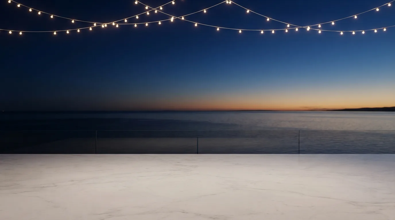 A marble terrace above the sea at dusk, strung with warm lights.